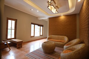 Una habitación amplia con pared de ladrillo, ventanas grandes, mobiliario de mimbre y una lámpara en el techo.