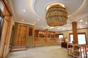 A spacious room with a high ceiling, a hanging light fixture, a wooden reception desk, and a brick wall. - The Grand View Ladakh (Leh)