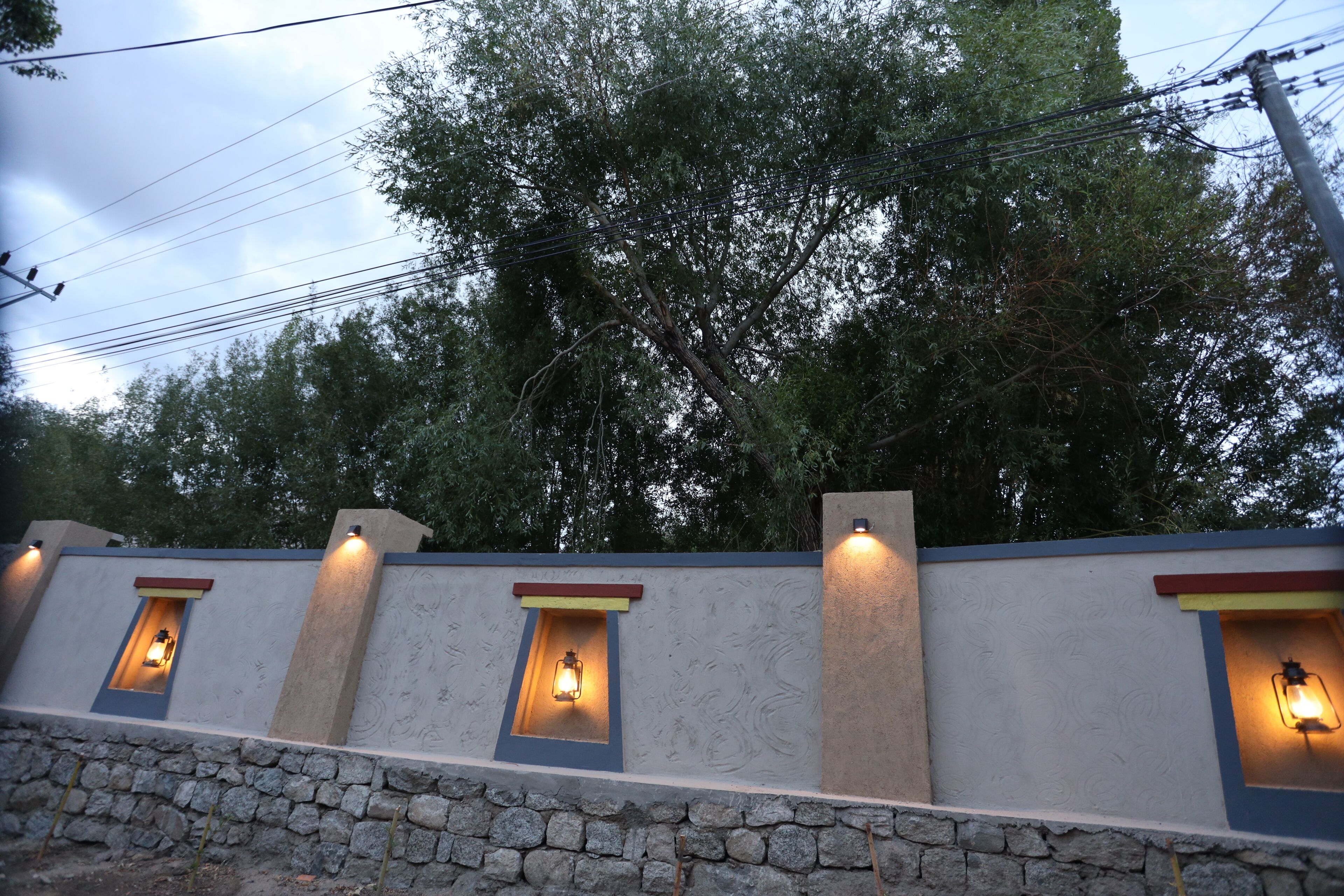 Un muro de piedra con luces empotradas y un árbol al fondo.