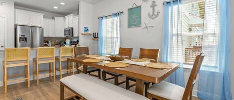 A modern kitchen with white cabinets, a stainless steel refrigerator, and a dining area with a wooden table and chairs.