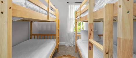 A room with bunk beds, a window with curtains, and a carpeted floor.