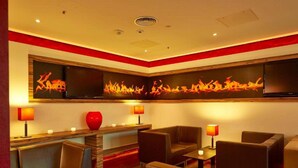 Un salón moderno con asientos de cuero, un florero rojo y televisores montados en la pared.
