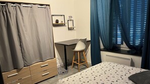 A bedroom with a bed, a desk, a chair, a wardrobe, and a window with curtains.