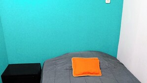 Een kamer met een bed, een klein zwart opbergvak en een witte stopcontact.