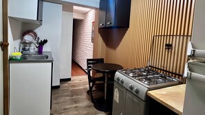 Een compacte keuken met een gasfornuis, een spoelbak en een eethoek met een stoel.