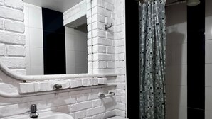 Een badkamer met een witte baksteenmuur, een wit wastafelmeubel, een toilet en een douchegordijn.