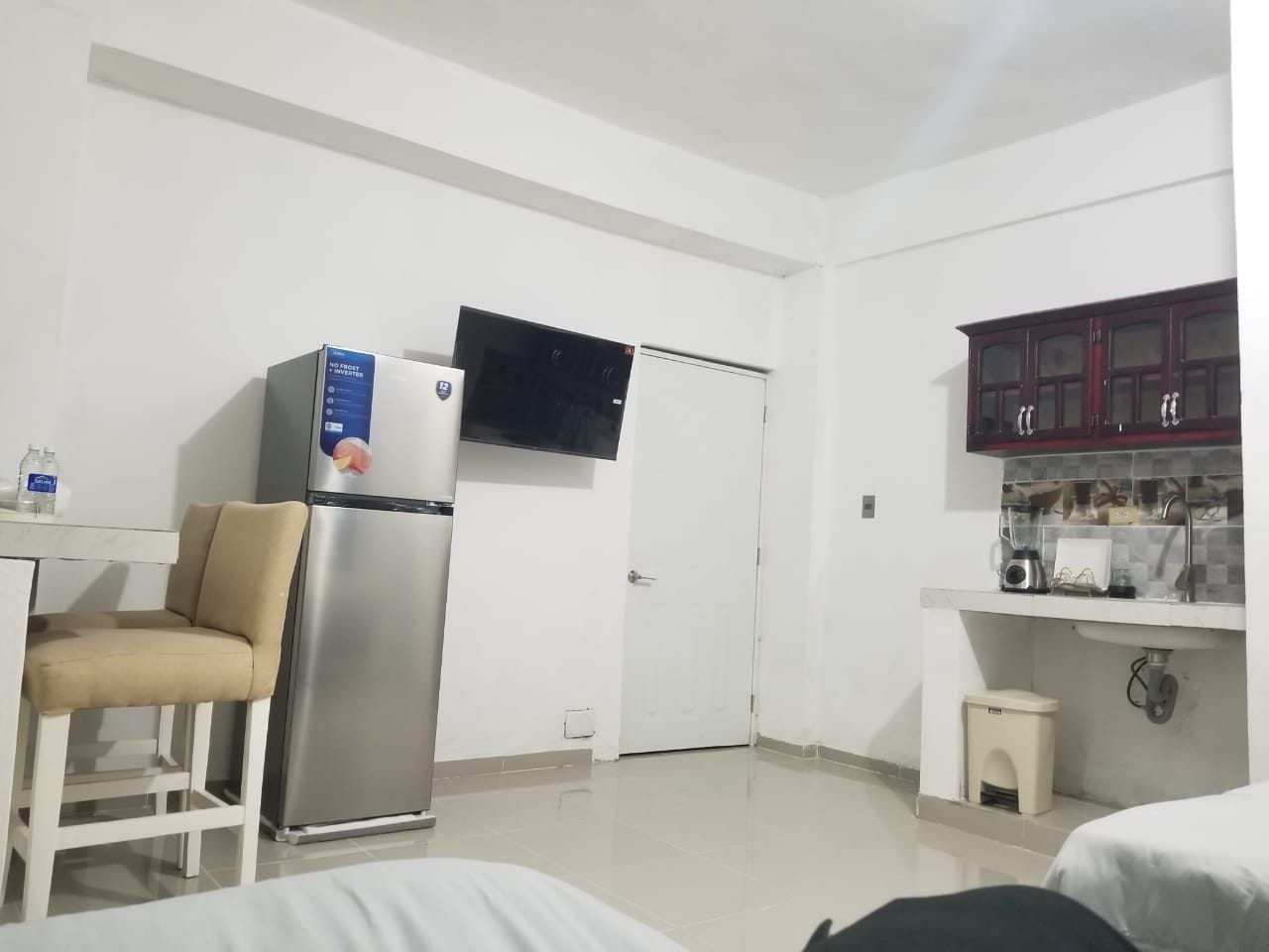 Une chambre d’hôtel compacte comprenant un coin cuisine, un lit, une chaise et un téléviseur fixé au-dessus de la porte.