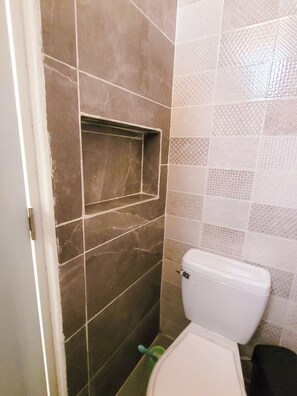 Un baño con inodoro, zona de ducha y pared con azulejos.