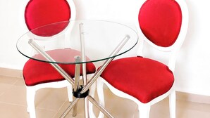A room with a flat-screen TV mounted on the wall, a glass table with metal legs, and two red upholstered chairs with white frames. - Yireh Hotel Grand Suites (San Juan de la Maguana)