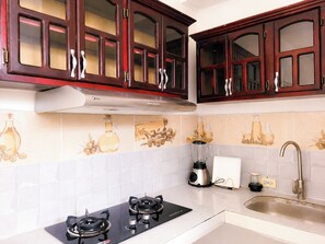 Una cocina con armarios de madera oscura, una campana extractora de acero inoxidable, una estufa a gas, una licuadora y un lavamanos.