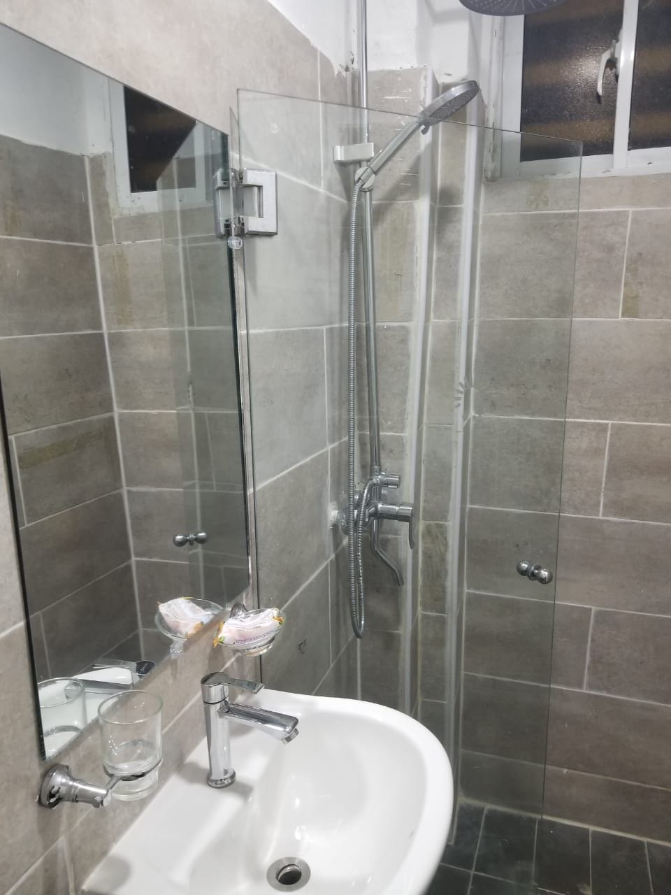 Un baño con ducha envuelta en vidrio, un lavamanos con un jabonera de vidrio y un espejo.