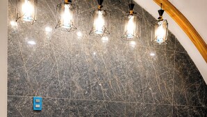 A reception area with a marble wall, a wooden reception desk, and hanging pendant lights. - Yireh Hotel Grand Suites (San Juan de la Maguana)