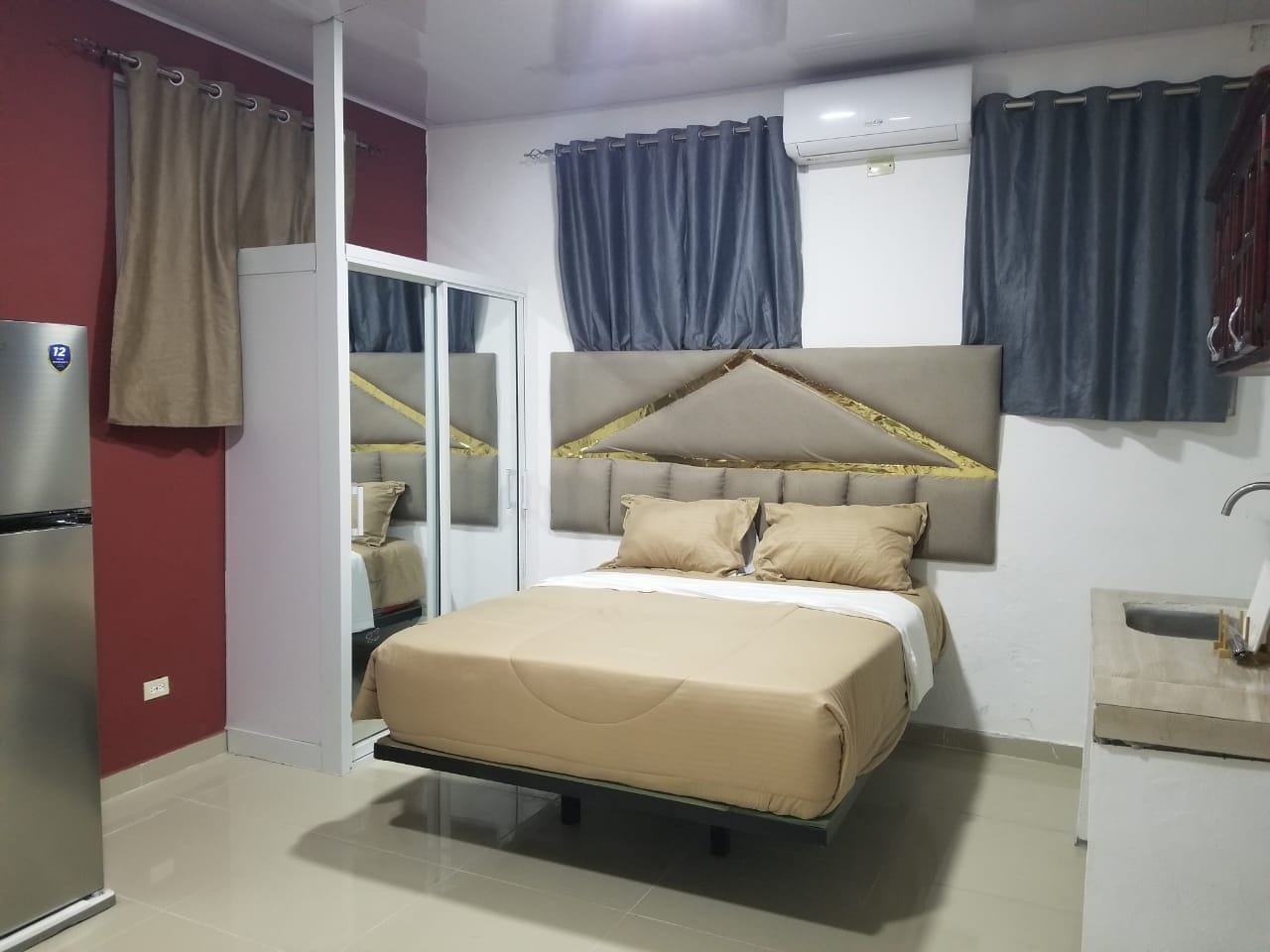Une chambre à coucher avec un lit, une armoire, un miroir, un lavabo et des rideaux.