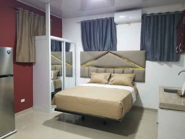 A bedroom with a bed, a wardrobe, a mirror, a sink, and curtains.