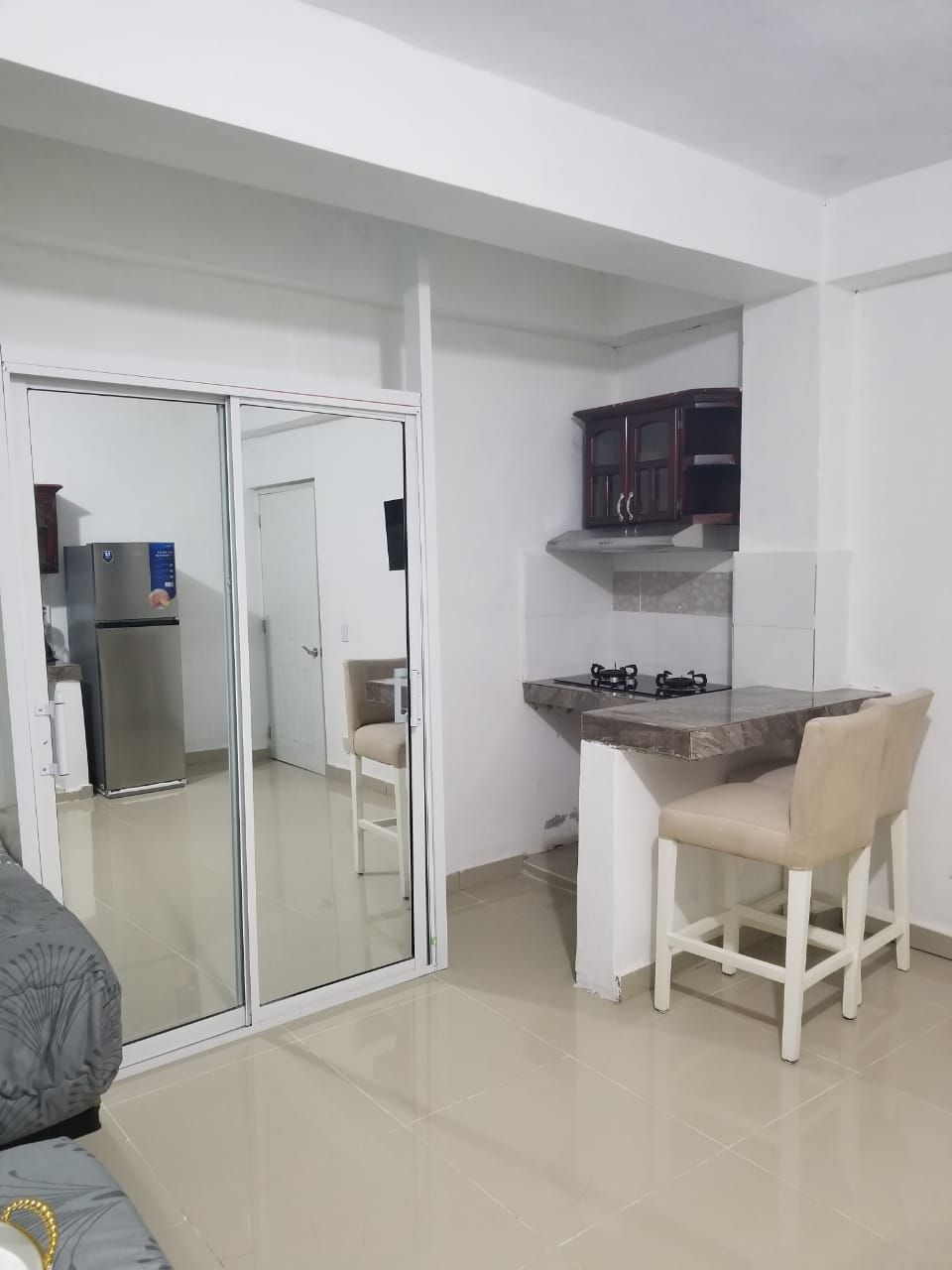 A compact living space with a kitchenette, a sliding glass door leading to another room, and a small dining area with a chair.