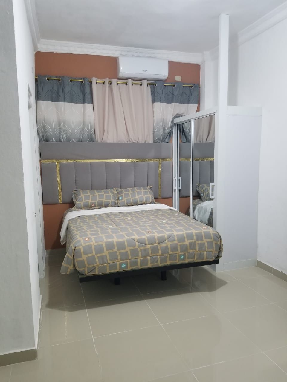 A bedroom with a bed, a headboard, a window with curtains, and an air conditioning unit.