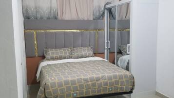 A bedroom with a bed, a headboard, a window with curtains, and an air conditioning unit.
