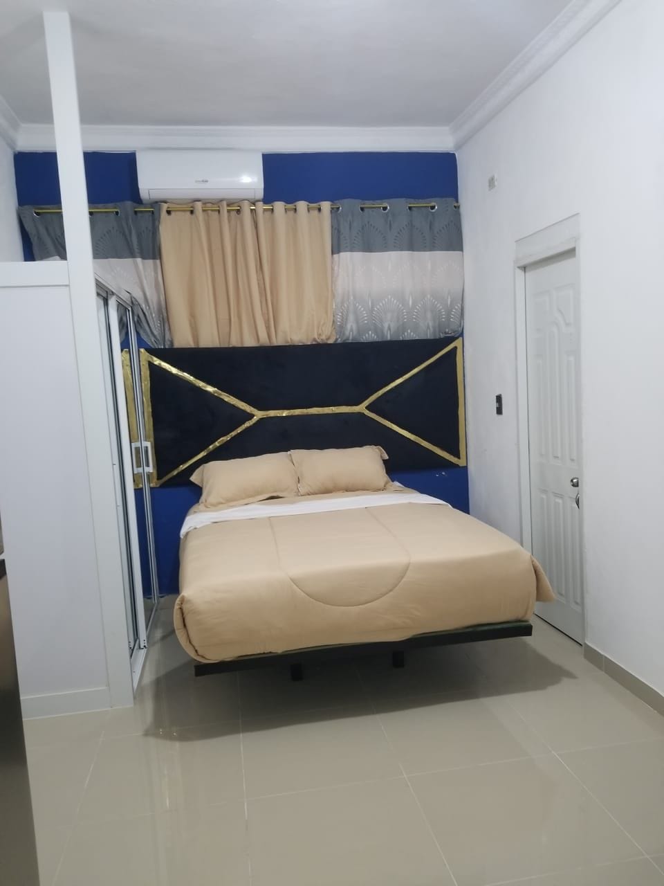 A bedroom with a bed, a wardrobe, a door, and an air conditioning unit.