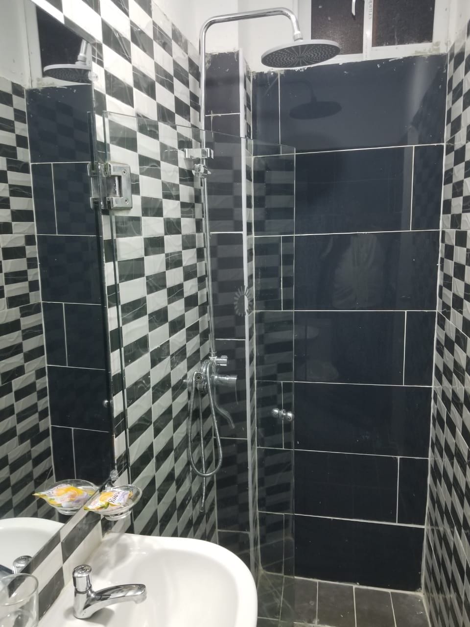A bathroom with a checkered black and white tile pattern, a glass shower enclosure, and a white sink with a faucet.