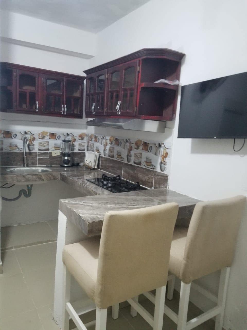 Cocina compacta con estufa a gas, dos sillas y un mueble empotrado.