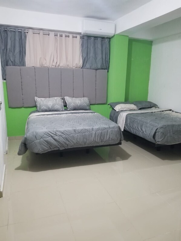 A room with two beds, a green accent wall, and a window with curtains.