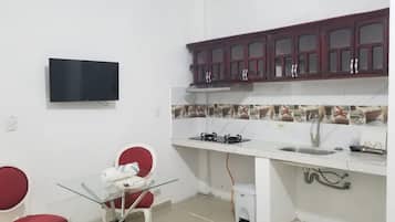 A compact kitchen with a TV, a dining area with two chairs, and a small trash bin.