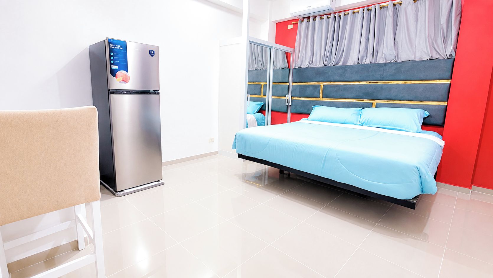 A modern hotel room with a bed, a seating area, and a refrigerator.