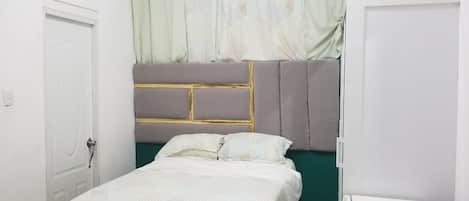 A bedroom with a bed, a white wardrobe, and a white cabinet.