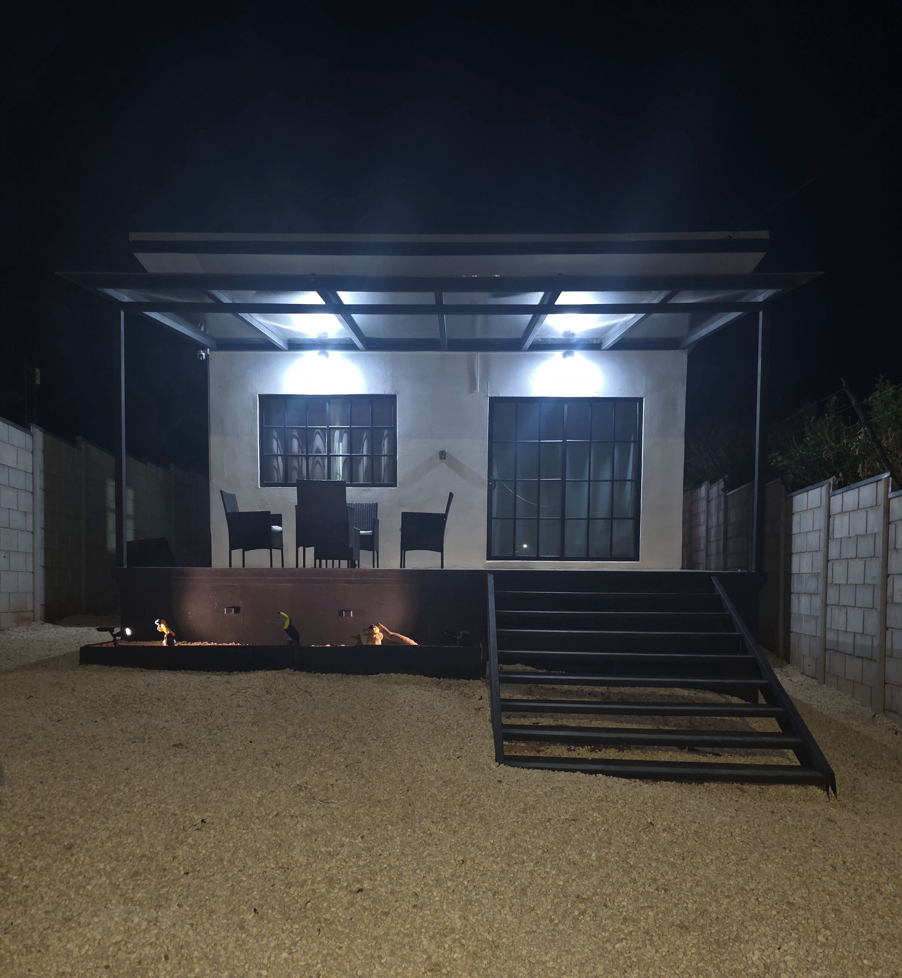 A modern outdoor structure with a covered seating area, a staircase, and a gravel ground.