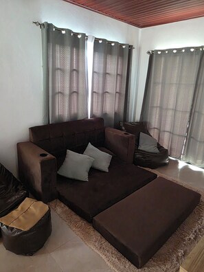 Ein Wohnzimmer mit einem braunen Sofa, einem passenden Ottomanen und einer kleinen schwarzen Mülltonne.
