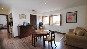 A living room with a sofa, a dining table with chairs, a kitchen area with a TV, and a window with a view. - Bright Village apartment, wrap around mountain views in Fornalutx.HighspeedWIFI (fornalutx)