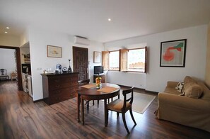 A living room with a sofa, a dining table with chairs, a kitchen area with a TV, and a window with a view. - Bright Village apartment, wrap around mountain views in Fornalutx.HighspeedWIFI (fornalutx)
