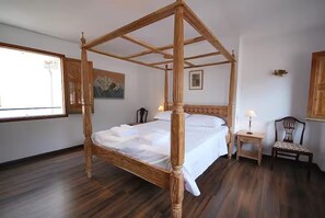 A four-poster bed in a room with wooden flooring, a small bedside table with a lamp, and a chair. - Bright Village apartment, wrap around mountain views in Fornalutx.HighspeedWIFI (fornalutx)