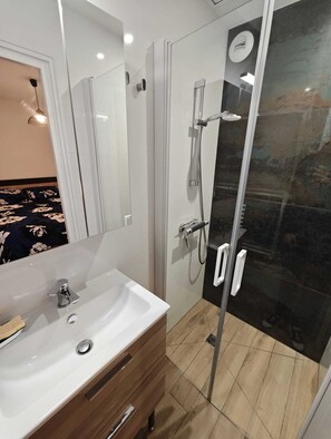 A modern bathroom with a glass shower enclosure, a white sink, and a wooden vanity. - Vrbo Property (Morlaix)