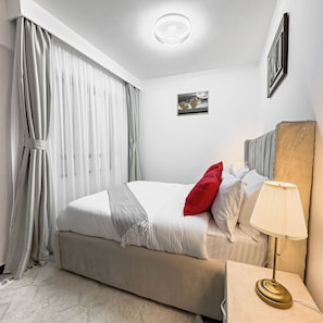 Una cama bien hecha con almohadas y una colcha, una lámpara de noche y un cuadro en la pared.