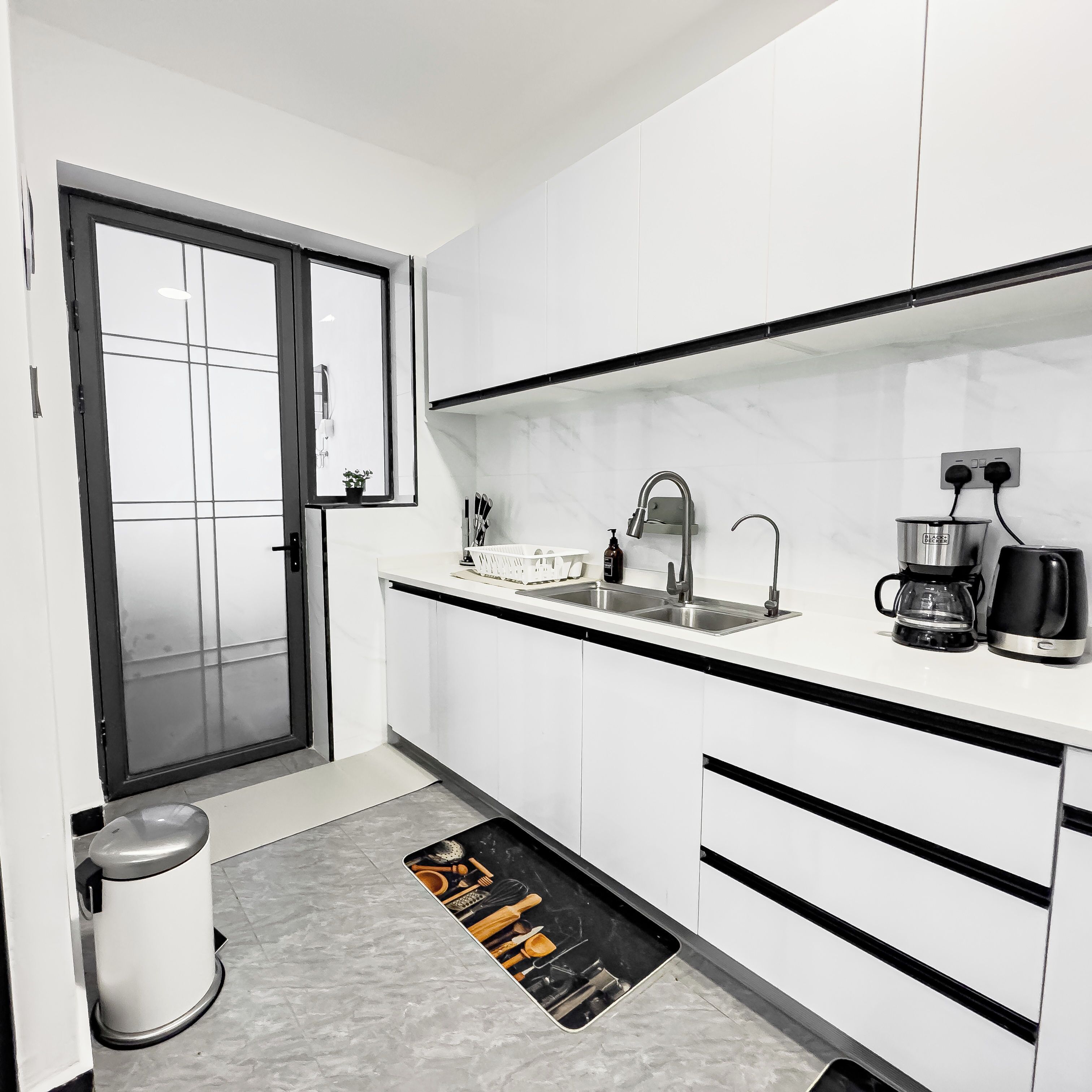 A modern kitchen with white cabinets, a stainless steel sink, and a coffee maker.