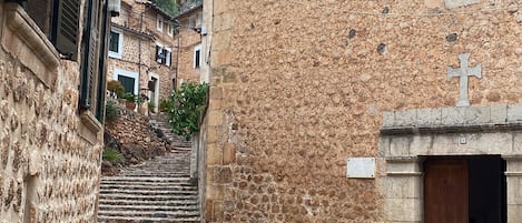 A cobblestone street leading to a stone building with a wooden door and a cross above it.