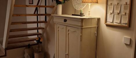 A staircase with wooden railings, a cabinet with a vase of flowers, a lamp, and a framed notice board.