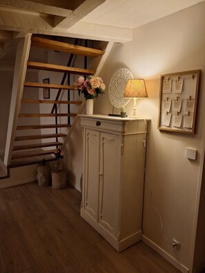 Una escalera con barandas de madera, un aparador con un florero, una lámpara y un tablón de anuncios enmarcado.
