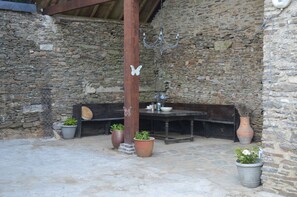 Un muro de piedra rústico, un banco de madera, una mesa con un florero y plantas en macetas.