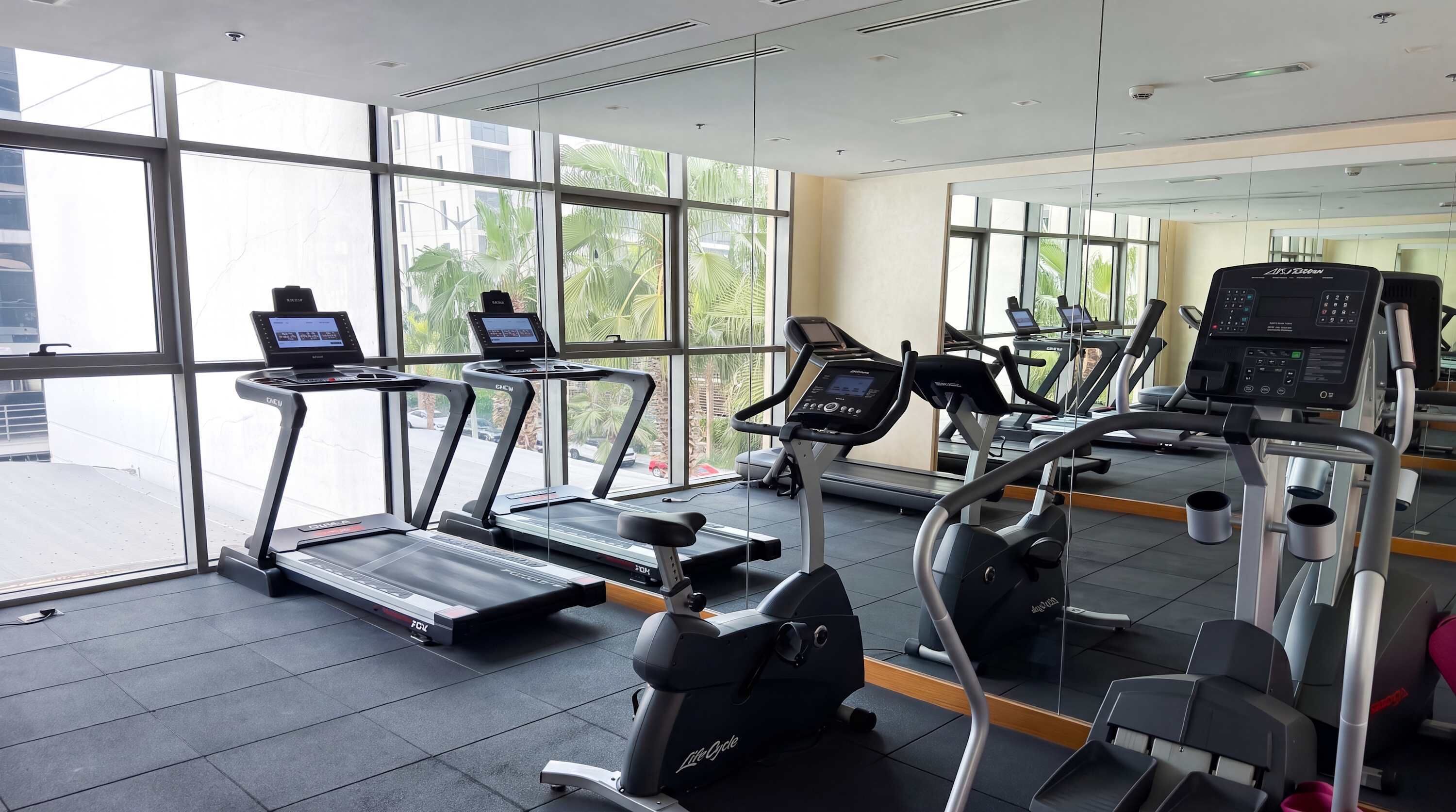 Un gimnasio con cintas de correr, bicicletas estáticas y un espejo grande.