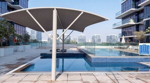 A rooftop swimming pool with a canopy, surrounded by modern buildings. - Stylish Studio in DAMAC Hills with Pool, Gym & Balcony (Damac hills)