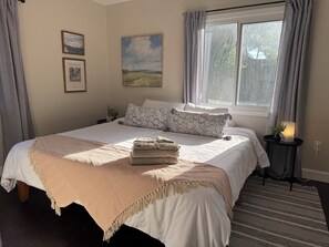 A neatly made bed with a beige blanket, a pillow with a floral pattern, and a landscape painting on the wall. - Beach Retreat - Hot Tub - 10 min Walk to Bay Beach (Fort Erie)