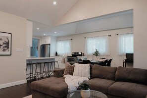 Un salon moderne avec un canapé marron, une table basse en verre et une cuisine en arrière-plan.