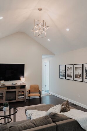 A modern living room with a flat-screen TV, a sofa, a chair, a coffee table, and a unique geometric ceiling light fixture. - Beach Retreat - Hot Tub - 10 min Walk to Bay Beach (Fort Erie)