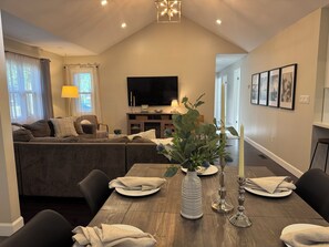 A living room with a sofa, TV, and dining table with chairs. - Beach Retreat - Hot Tub - 10 min Walk to Bay Beach (Fort Erie)