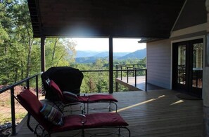 Ein überdachter Außenbereich mit zwei Sitzgelegenheiten und Blick auf eine gebirgige Landschaft.