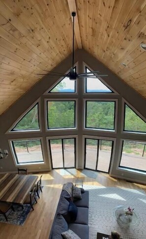Ein Zimmer mit schrägem Dach, großen Fenstern, einer Couch und einem Esstisch.