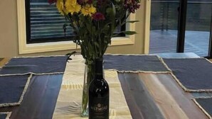 Une pièce avec une grande fenêtre, un vase rempli de fleurs et une bouteille de vin posée sur une table.