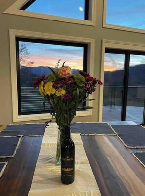 Ein Zimmer mit großem Fenster, einer Blumenvase und einer Weinflasche auf einem Tisch.